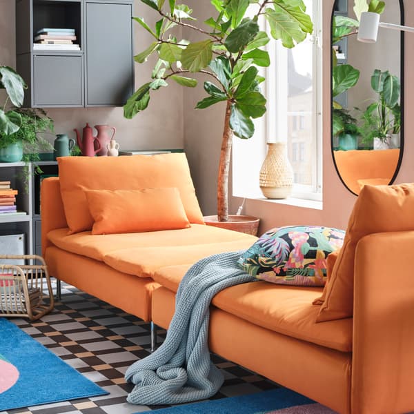 Two orange chaise longues are standing together to create a spacious day-bed, and a blue throw and a floral cushion lie here.