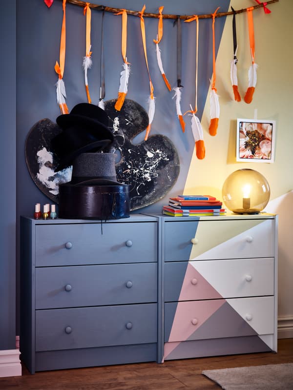 Two painted chest of drawers in pink/blue-grey/yellow/white, a grey table lamp and a black table lamp.