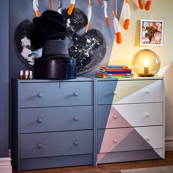 Two painted chest of drawers in pink/blue-grey/yellow/white, a grey table lamp and a black table lamp.