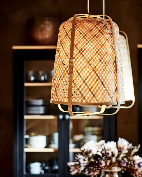 Two pendant lamps in bamboo are lit and give a soft-glowing light. A HEMNES glass-door cabinet stands in the background.