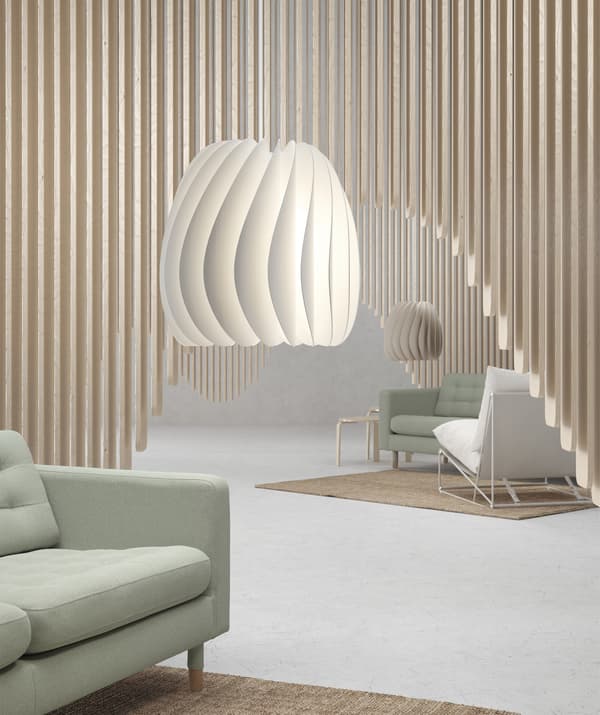 Two pendant lampshades hanging in a room with  pale green sofas and wooden panelled decoration.