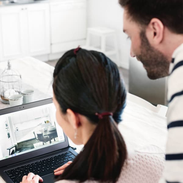 Two people are looking at a laptop in a kitchen.