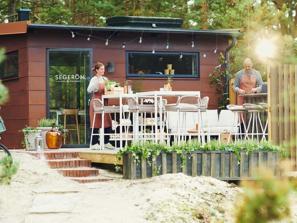 Two people are setting up an outdoor pop-up restaurant in the forest consisting of SEGERÖN outdoor furniture.