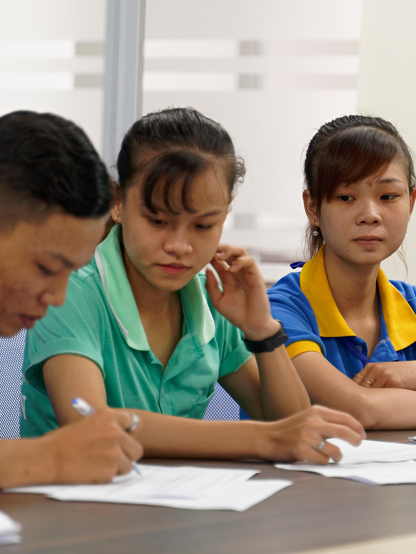 Two people at an IKEA supplier somewhere in Asia sitting at a desk watching as a third person fills in a form.