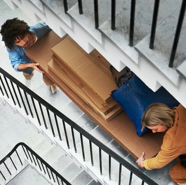 Two people carry packages up the stairs.