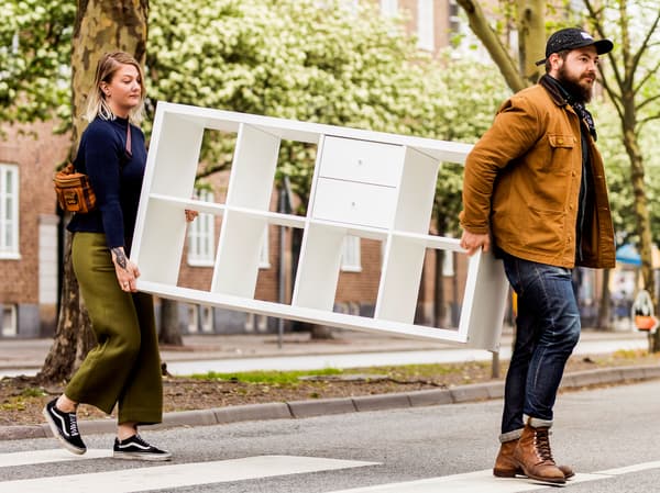 Two people carrying KALLAX across the street