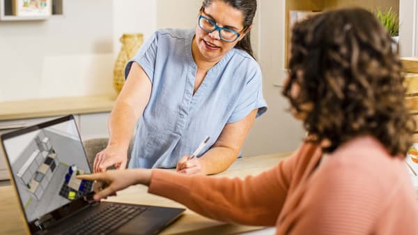 Two people discussing a 3D room layout displayed on a laptop screen.