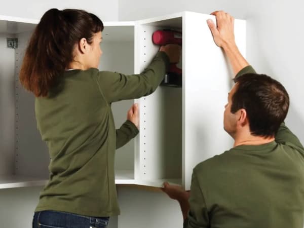 Two people installing a kitchen compartment