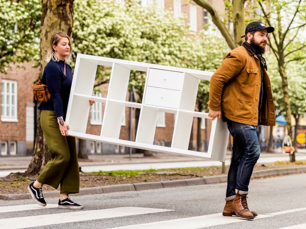 Two people moving a KALLAX shelf across a street.