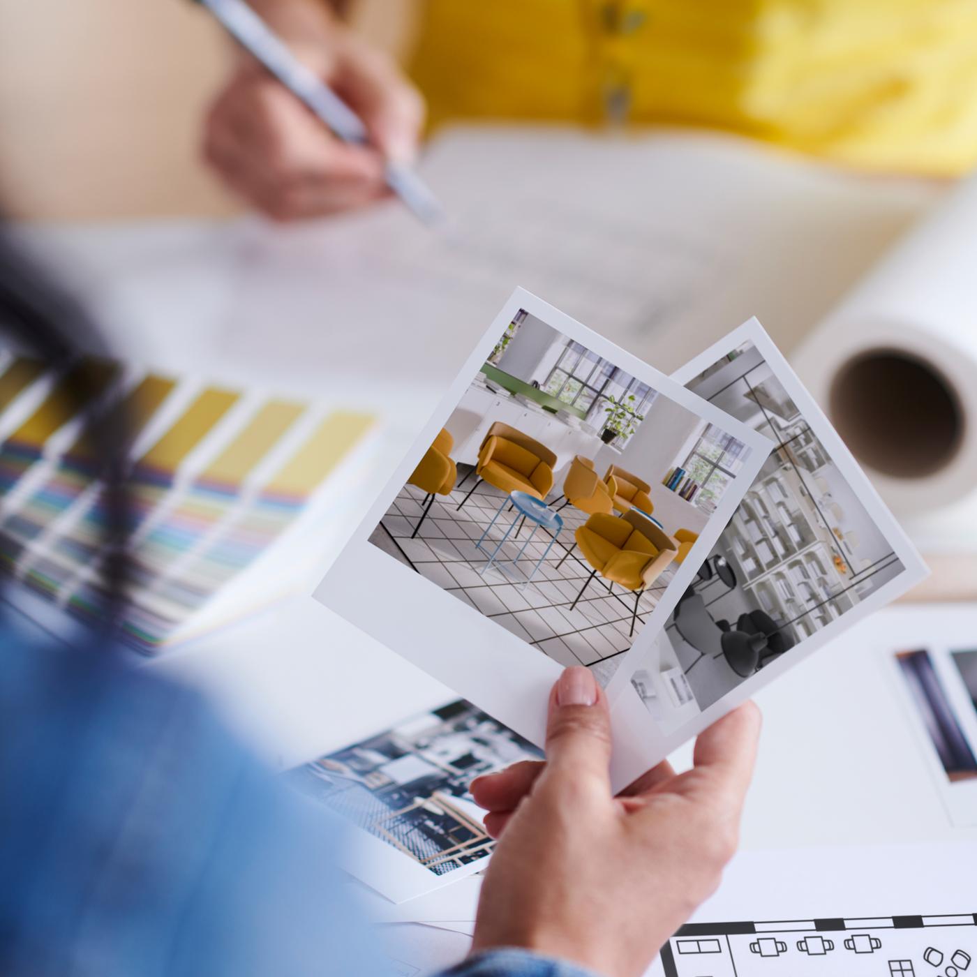Two people on opposite sides of a tabletop with colour swatches, room sketches and a floor plan scattered on it.