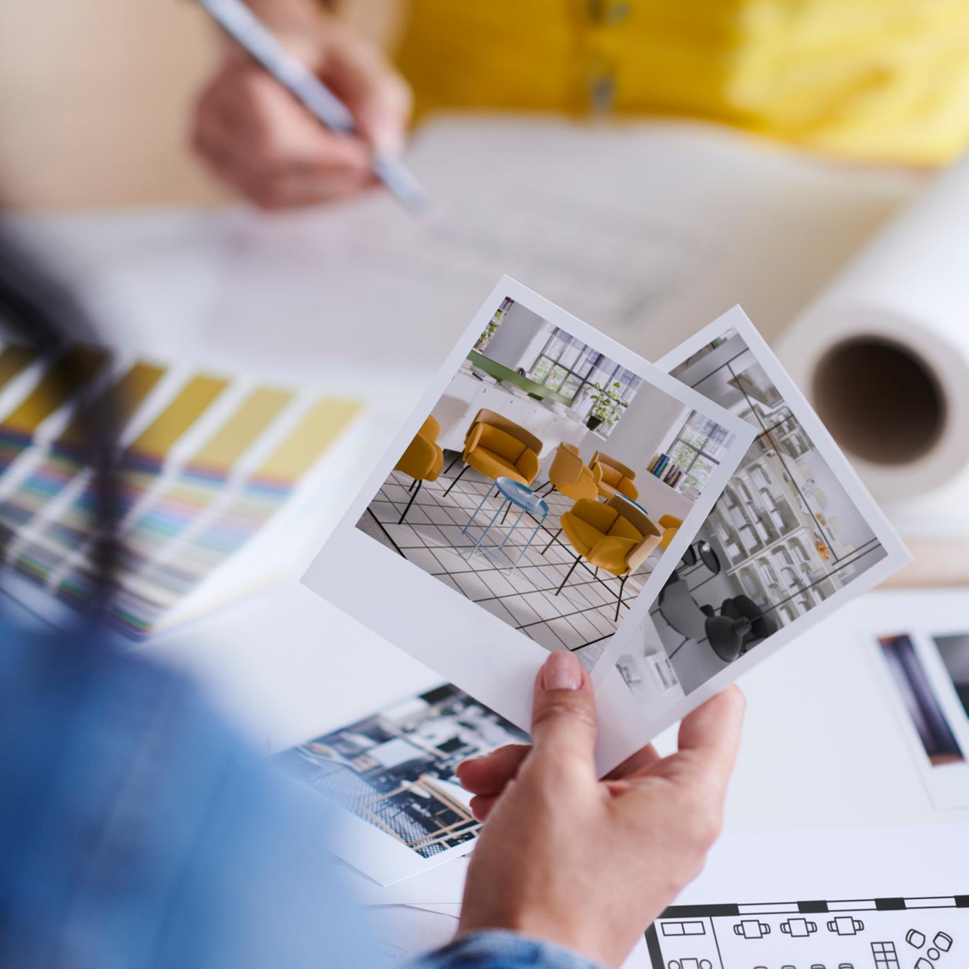 Two people on opposite sides of a tabletop with colour swatches, room sketches and a floor plan scattered on it.