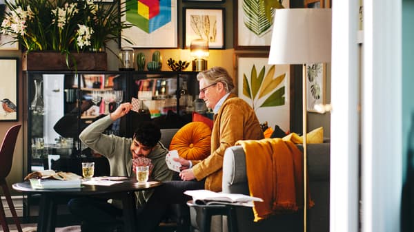 Two people playing cards on a black KRAGSTA coffee table with a gallery wall behind them with assorted framed BILD posters.