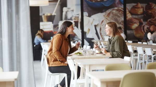 Two people seated at a café table, talking over drinks in a bright, modern dining space