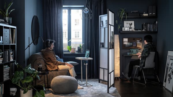 Two people seated at opposite sides of a living room, separated by a RISÖR room divider, both focusing on their screens.