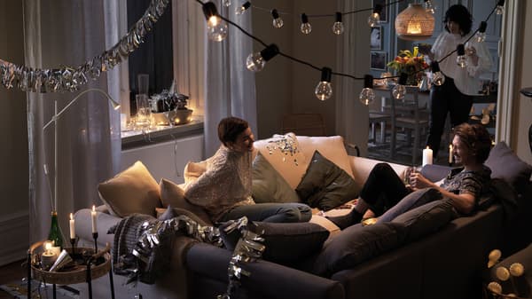 Two people sit together in two sofas that have been pushed together in the middle of a room, laughing and chatting.