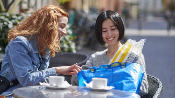 Two people sitting at a table outside with a blue bag full of IKEA product.