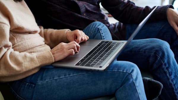 Two people sitting on a sofa, one of them has an open laptop on his lap