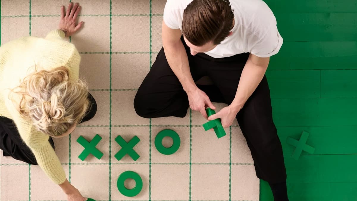 Two people sitting on the carpet playing with large X and O blocks. 