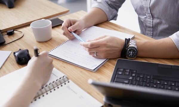 Two people sitting opposite each other with open notebooks and laptops.