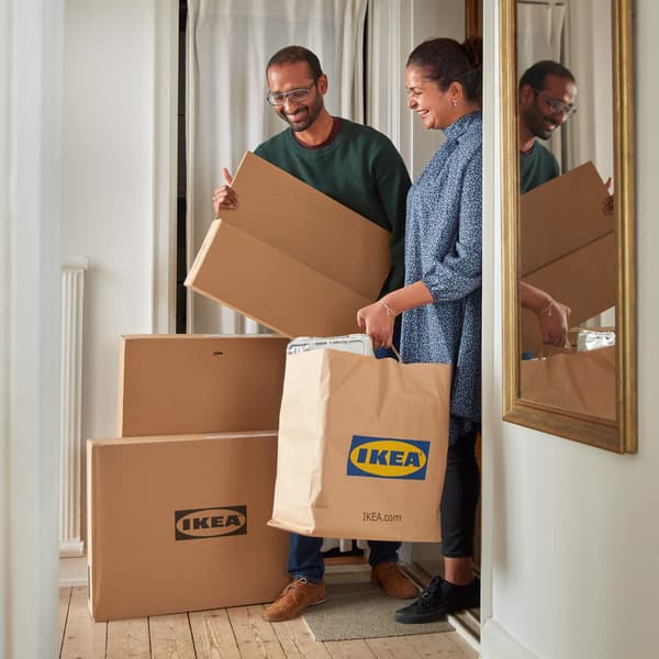 Two people smiling and bringing IKEA boxes and bags into their home.