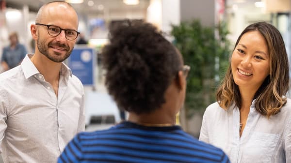 Two people smiling at an IKEA co-worker wearing a blue shirt with 'Hej!' on the back of it
