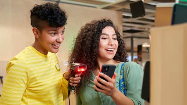 Two people standing next to each other. An IKEA co-worker scans a coupon on a customer’s smartphone with a handheld scanner.
