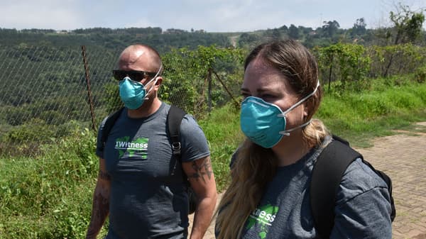Two people wearing blue masks walk down a dirt path.