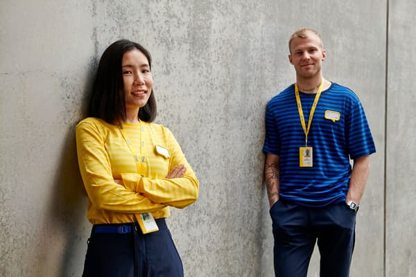Two people with ID badges stand in front of a concrete wall