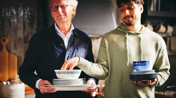 Two people with one of them holding a stack of white UPPLAGA serving and side plates and a white/patterned FRIKOSTIG bowl.
