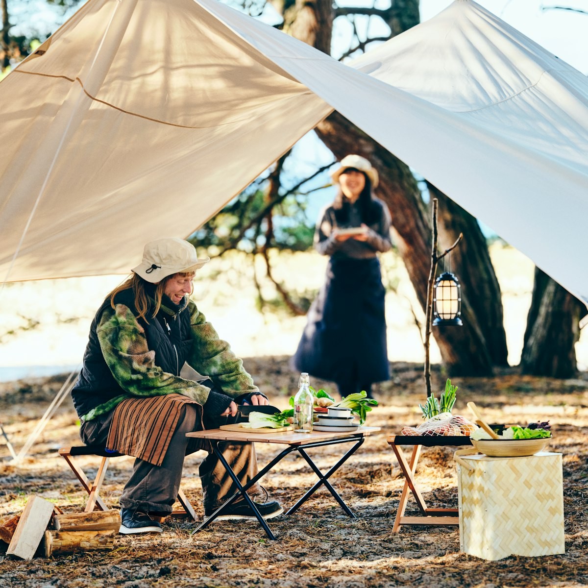Two persons are in a campsite with a SOLUPPGÅNG folding table made, set up for a meal under the canopy.