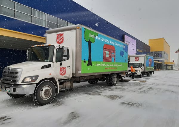Two Salvation Army trucks outside an IKEA store on a snowy day.
