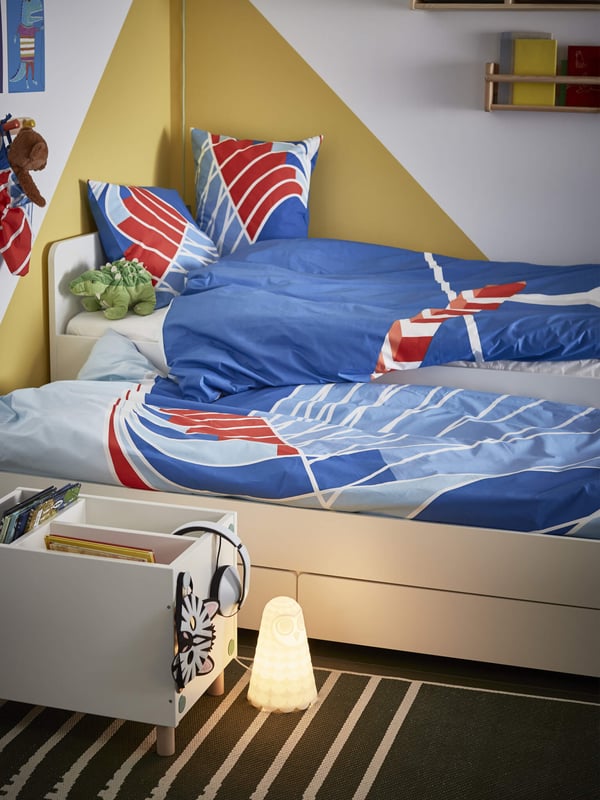 Two single beds side by side with a blue, red and white patterned duvet and pillows, linking to the kids furniture page.