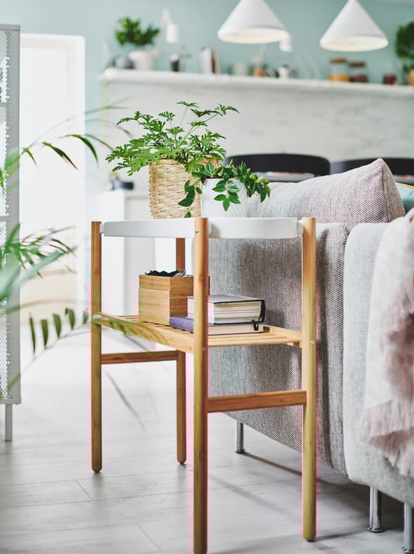 Two small, potted plants along with very light storage on a SATSUMAS plant stand placed next to a living-room sofa.