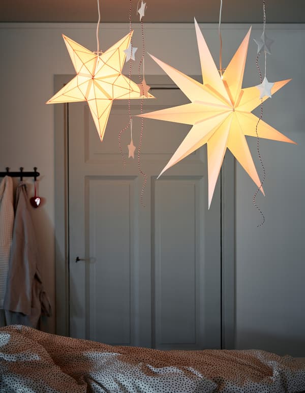 Two star-shaped paper pendant lamps on HEMMA cord sets with rail, hanging from the ceiling and over a bed.