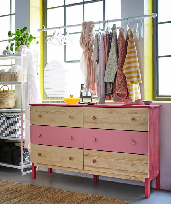 Two TARVA solid wood chest of drawers, with the middle drawers painted pink. Clothes hang above on a rod.