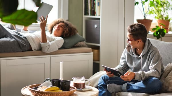 Two teens relaxing in a living area, with one sitting behind a birch veneer BORGEBY coffee table on a SÖDERHAMN 3-seat sofa.