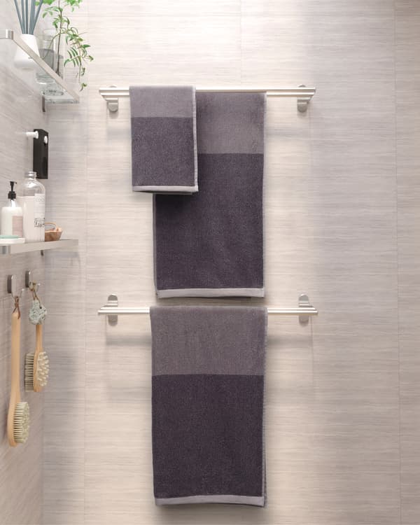 Two towel rails in stainless steel are mounted on a wall. On the wall next to it are glass shelves with shower products.