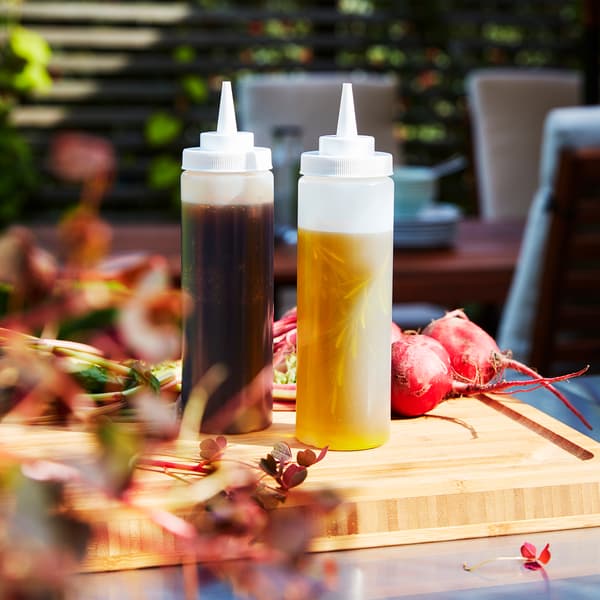 Two transparent squeeze bottles stand on a wooden chopping board. There’s oil in one bottle and marinade in the other.