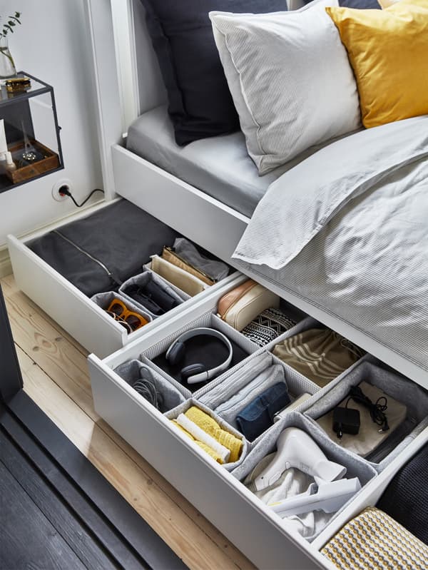 Two under-bed storage boxes, pulled out to reveal neatly organised bedroom accessories in grey IKEA RAGGISAR baskets.