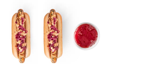 Two vegetable hot dogs with fried onions and cabbage, a full glass of red drink.