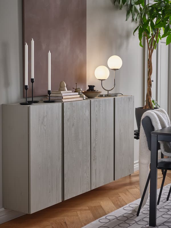 Two wall-mounted and grey-painted IVAR cabinets with candles, books, decorations and a chrome-plated table lamp on top.