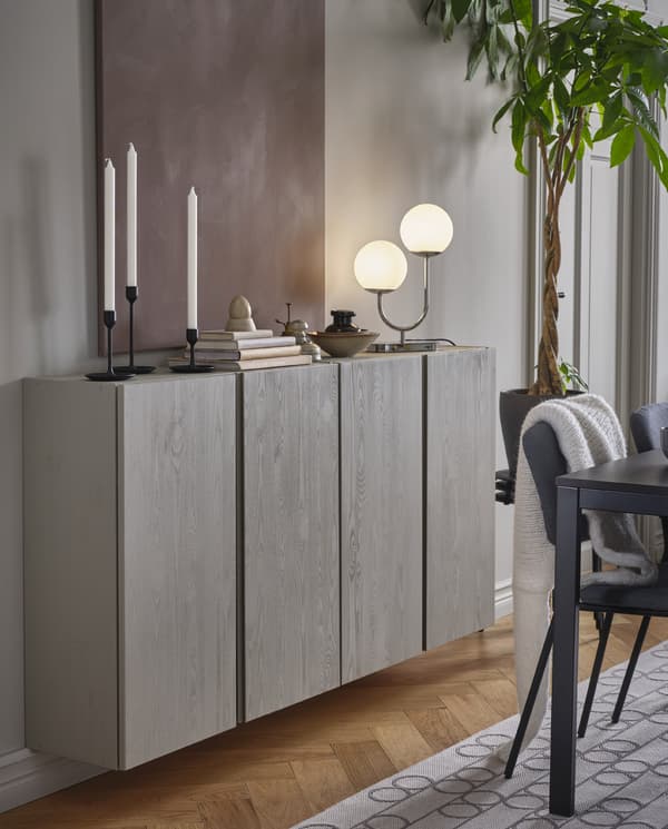 Two wall-mounted and grey-painted IVAR cabinets with candles, books, decorations and a chrome-plated table lamp on top.