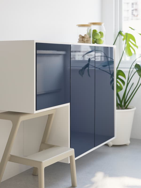 Two wall-mounted cabinets, one large and one small, with glossy black-blue doors. A step stool is below the smaller cabinet.