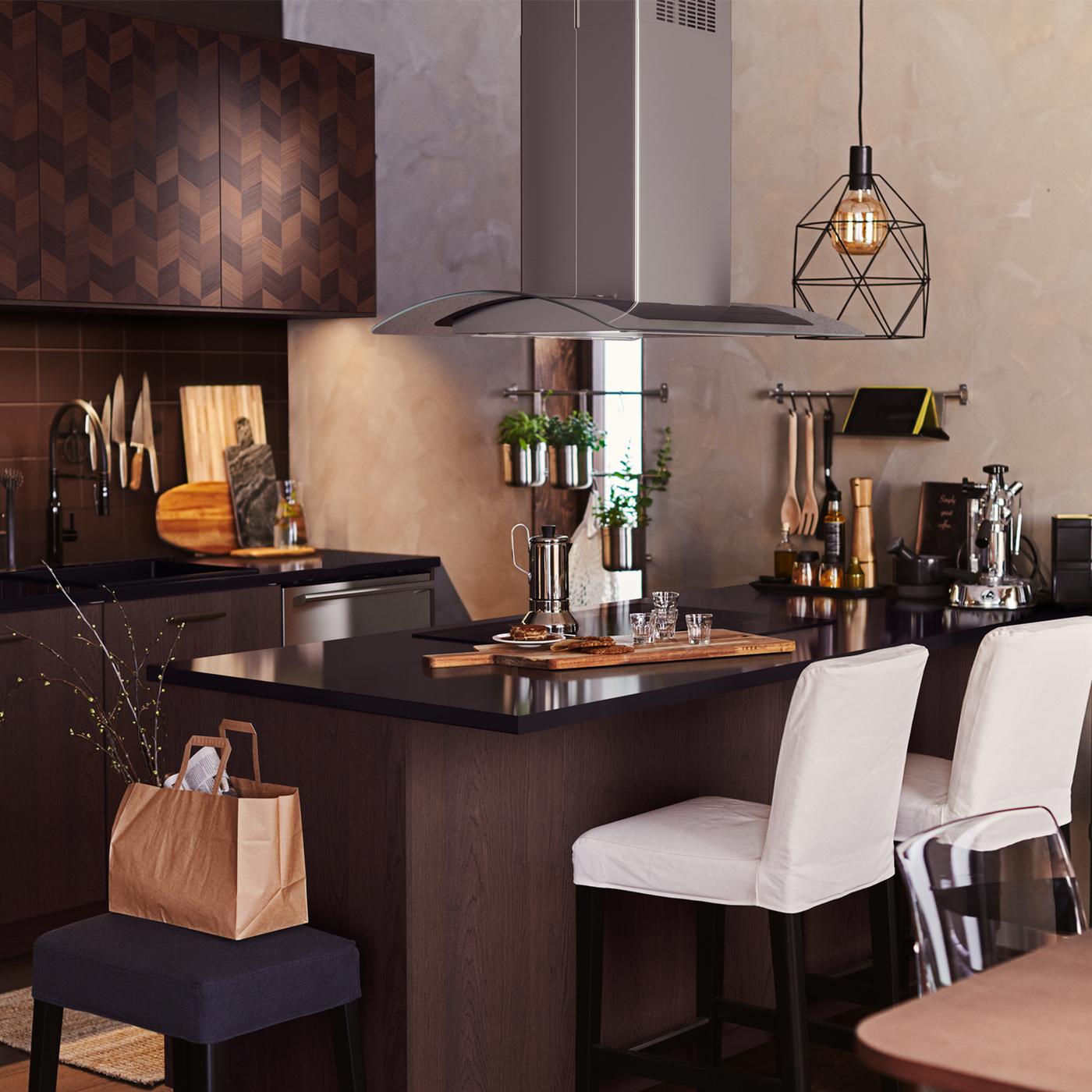 Two white BERGMUND bar stools at an island worktop under a BRUNSTA pendant lamp in a brown SINARP/HASSLARP kitchen.