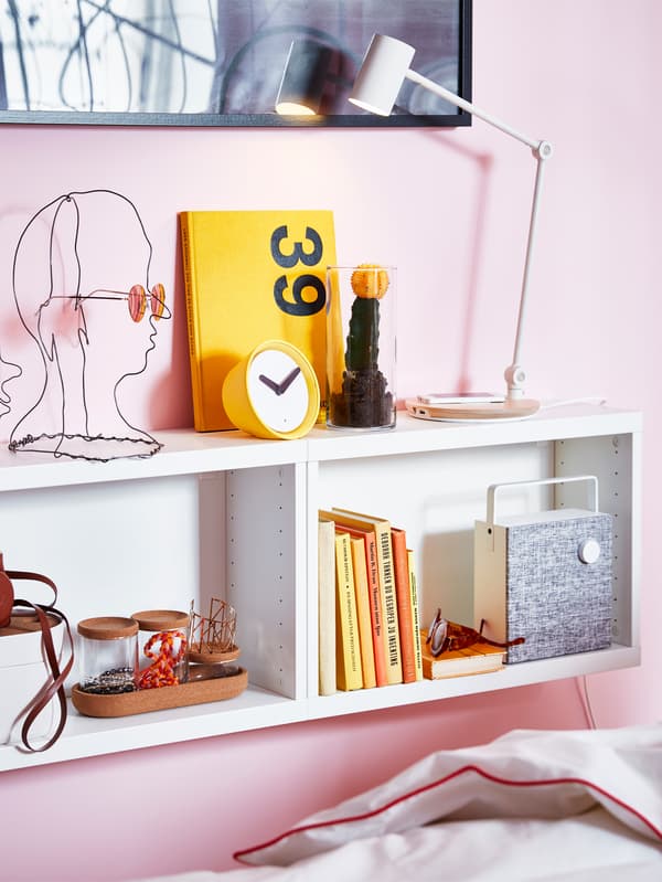 Two white BESTÅ frames mounted on a pink wall, decorated with magazines, a table lamp, an ENEBY speaker and decorative objects.