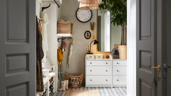 Two white HAUGA chests of 3 drawers stand in a hallway with a RÅMEBO mirror and a large wall clock on the wall.