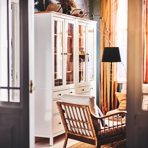 Two white HEMNES glass-door cabinets with three drawers, with four TVÄRDRAG cabinet lights on top, and an armchair on a rug.