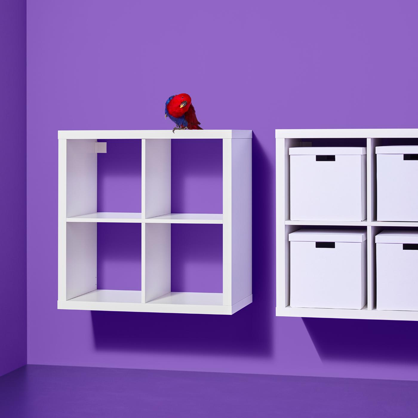 Two white KALLAX shelving units, one containing white boxes, are mounted side by side on a purple wall.