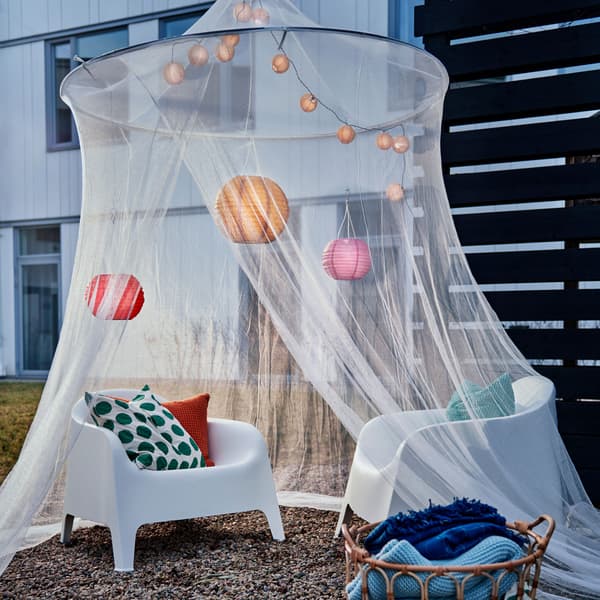 Two white plastic chairs within a white hanging mosquito net adorned with string lights and lanterns.