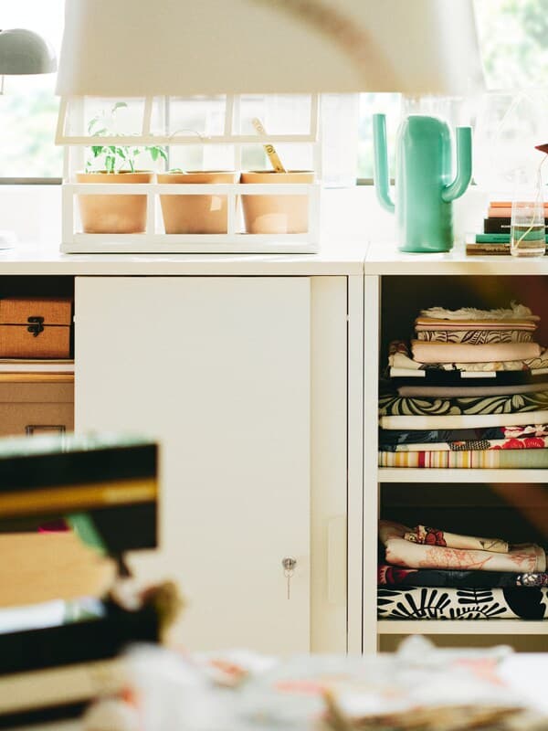 Two white TROTTEN cabinets with sliding doors with a bright green ÄRTBUSKE vase/watering can on top of one of them.
